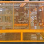 Industrial machinery behind yellow safety guard fencing in factory setting