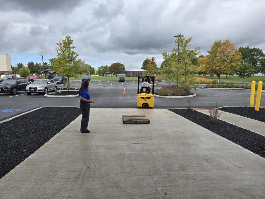 Forklift operator approaching pallet while worker observes in outdoor loading area