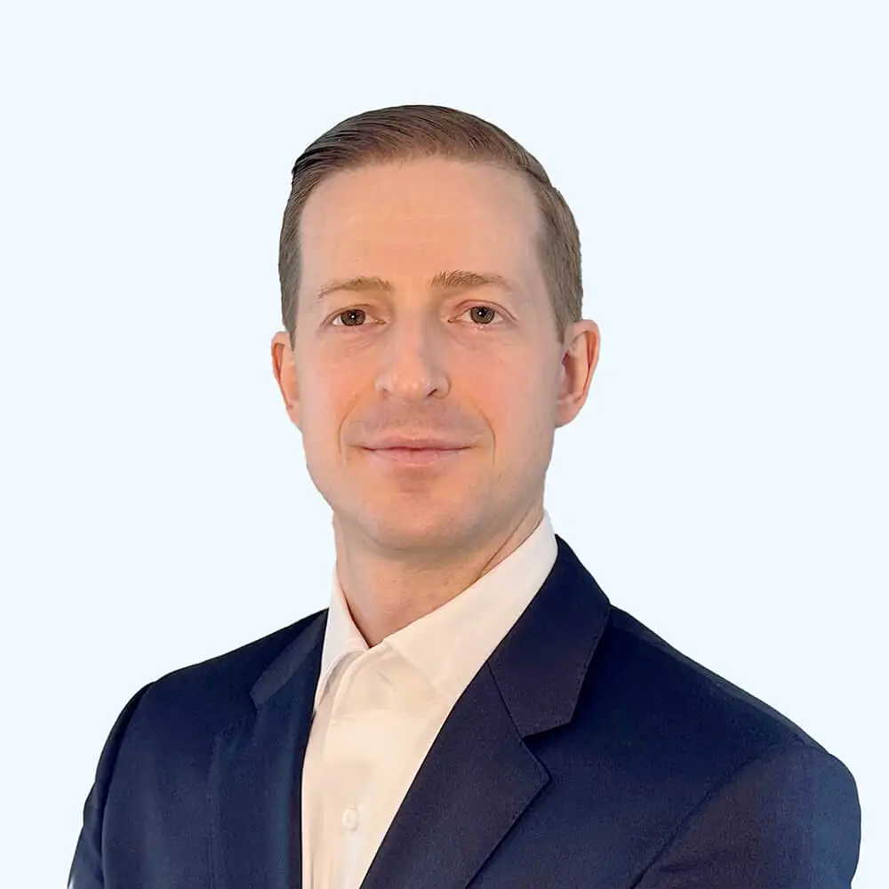 Portrait of a man with neatly styled light brown hair, wearing a navy suit jacket and white dress shirt, facing the camera against a clean, light background.