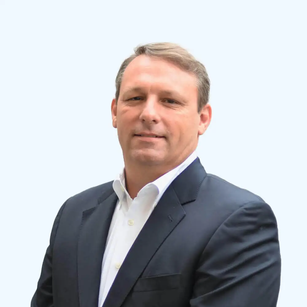 Portrait of a man with short light brown hair wearing a dark suit jacket and white dress shirt, facing the camera against a clean, light background.