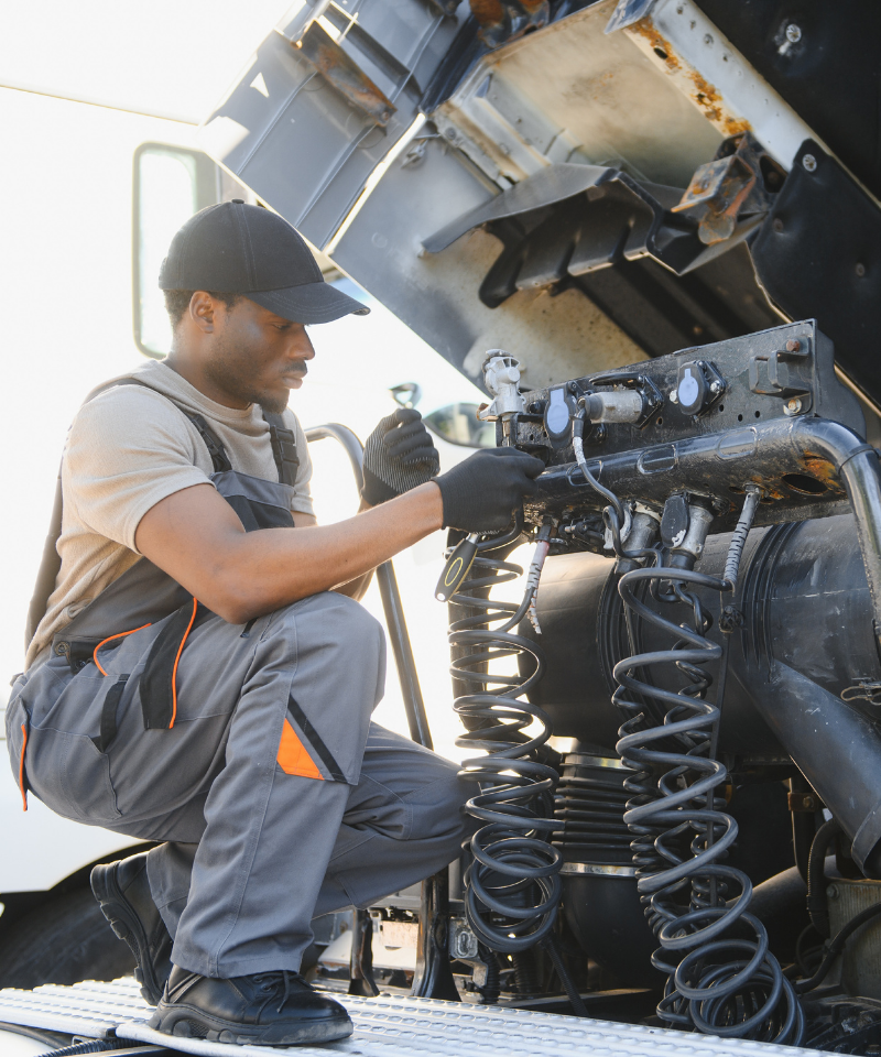 Worker in overalls inspecting and repairing truck equipment with tools