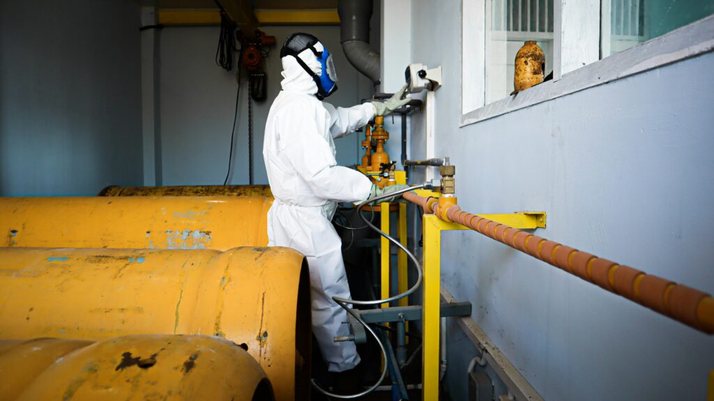 Worker in hazmat suit operating gas pipes and control valves indoors