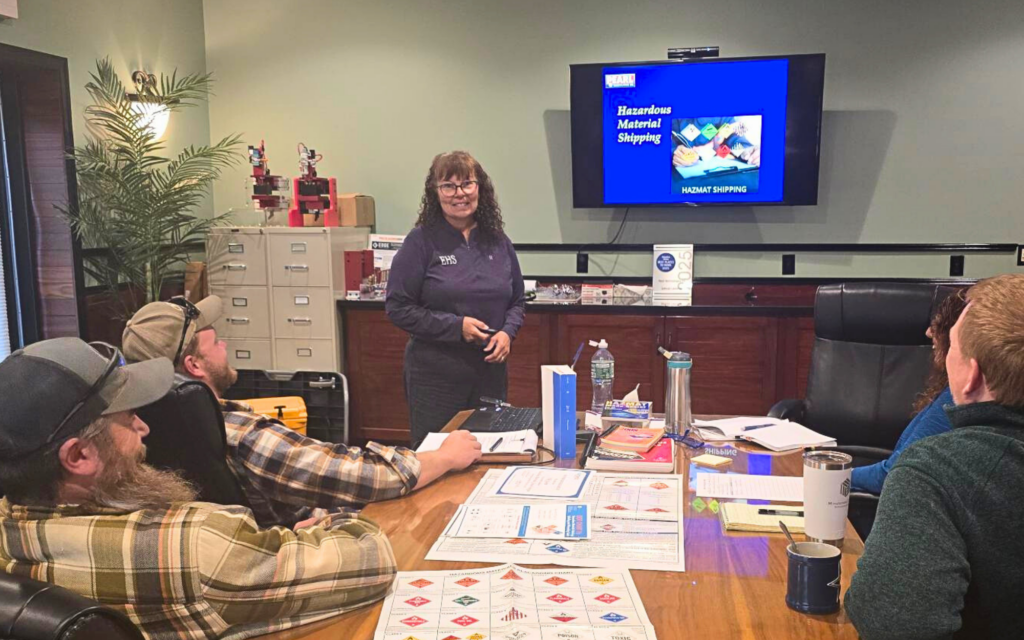 Trainer leading hazardous materials shipping meeting with team in conference room