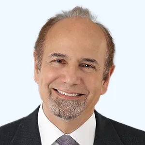 Portrait of a smiling man with short thinning hair and a neatly trimmed goatee, wearing a suit jacket, dress shirt, and tie against a light background.