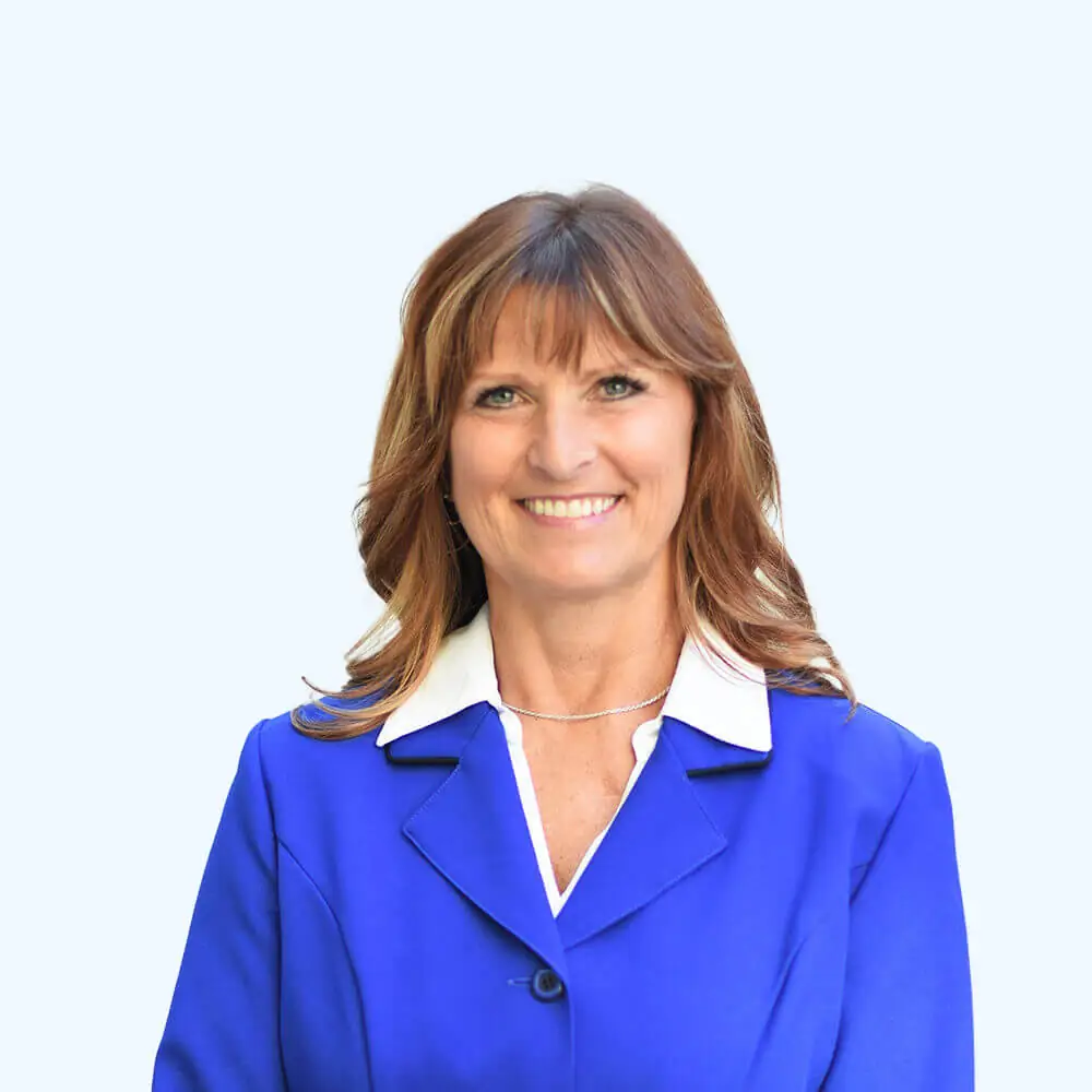 Portrait of a smiling woman with shoulder-length brown hair and bangs, wearing a bright blue blazer and white collared shirt against a clean, light background.