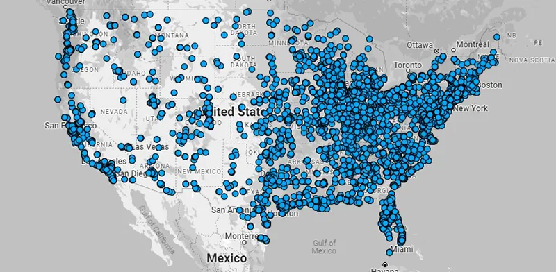 A grayscale map of the United States covered with hundreds of blue dots indicating data points or facilities, densely concentrated in the eastern half and southeastern states, with fewer points in the western regions.