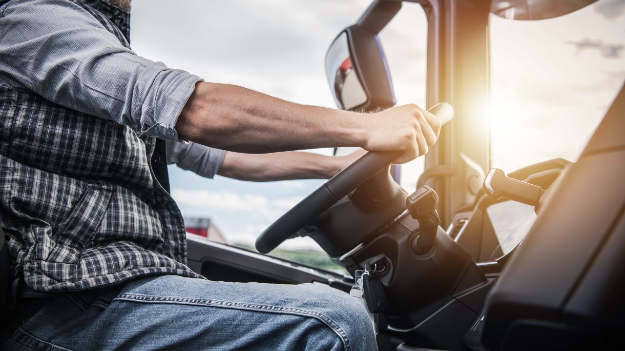 Truck driver with hands on steering wheel and sun shining through windows