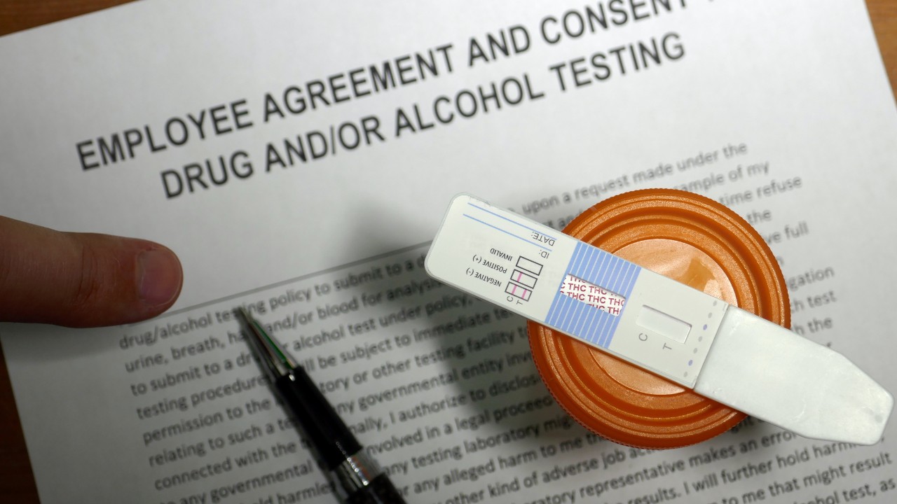 Drug test strip and cup sitting atop an employee agreement document